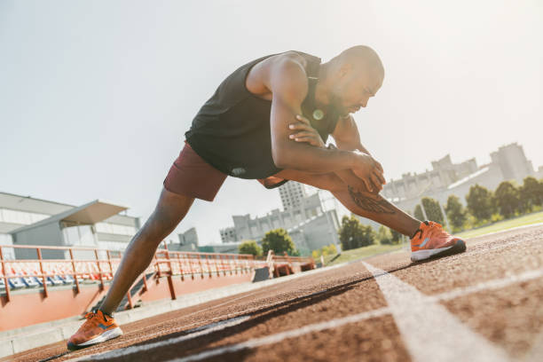 istock Male runner stretching legs preparing for run training on stadium tracks doing warm-up exercises 1174864548