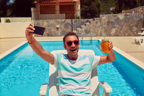 istock Attractive man using cellphone while drinking juice near swimming pool. 1174864762