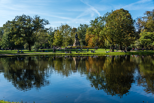 Amsterdam, Holland, August 2019 Reflections at Amsterdam Vondelpark during autumn with trees in beautiful colors reflecting in the water and a statue of Joost van den Vondel