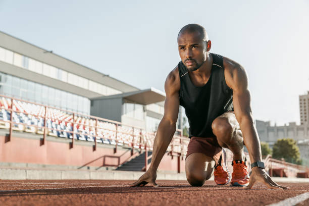 vista de ángulo bajo del joven atleta en posición de salida para correr en la pista deportiva - atletismo en pista masculino fotografías e imágenes de stock