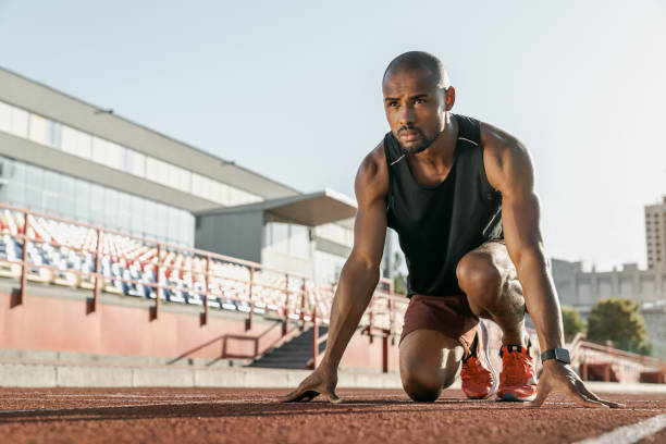 Low angle view of young man athlete in starting position for running on sports track Running, Sport, Sprinting, Athlete, Exercising mens track stock pictures, royalty-free photos & images