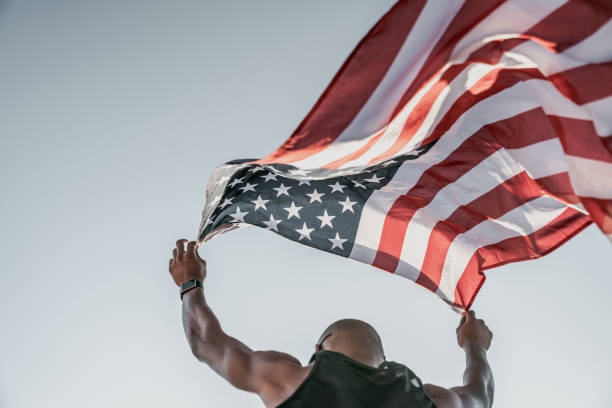 머리 위에 미국 국기를 들고 운동 트랙에서 달리는 선수의 낮은 각도보기 - american sports 뉴스 사진 이미지