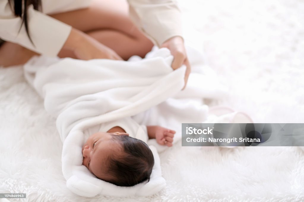 Newborn baby was swaddling with white cloth by her mother and the activity is on bed Newborn baby was swaddling with white cloth by her mother and the activity is on bed. Baby Blanket Stock Photo