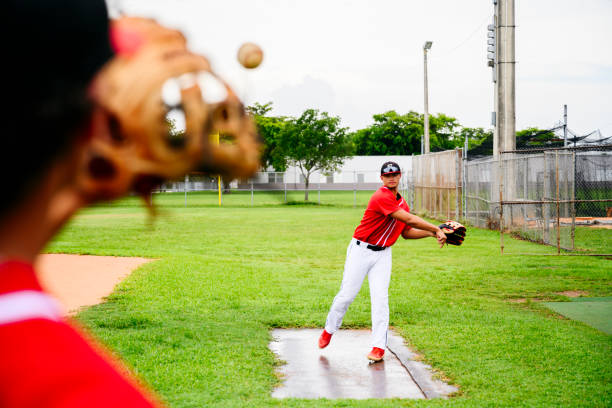 Young Hispanic baseball players warming up before game Over the shoulder viewpoint of young Hispanic baseball players throwing the ball around and warming up before game. high school baseball stock pictures, royalty-free photos & images