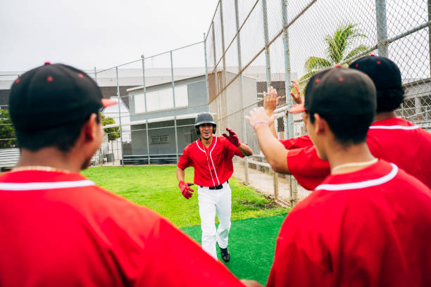 istock Scoring baseball player running toward teammate high-fives 1174867079