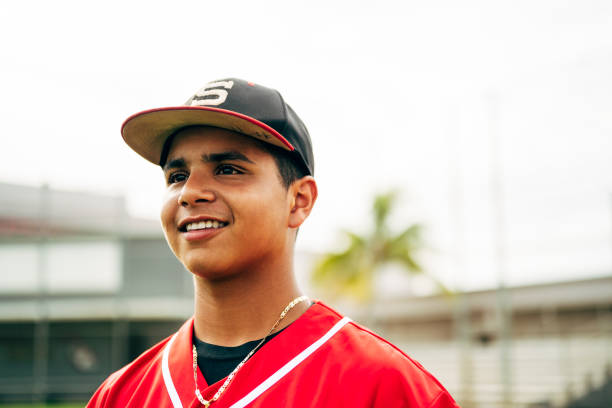 Close-up of smiling Hispanic baseball player looking away Portrait of smiling teenage Hispanic baseball player suited up and standing outdoors waiting to play. high school baseball stock pictures, royalty-free photos & images