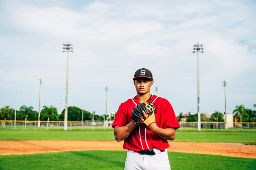 Wide-angle portrait of young Hispanic baseball pitcher standing on the mound with ball in glove and ready for his next pitch.