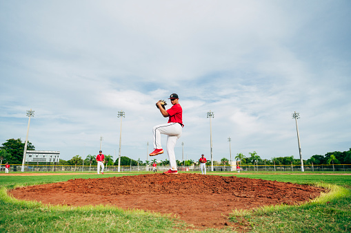 Low angle view of Hispanic baseball pitcher standing on the mound in wind-up position preparing to throw the ball.