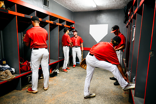 Young Hispanic baseball team members in uniform standing in locker room and talking before taking the field for a game.