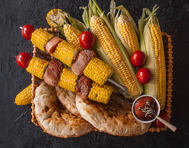 黒い暗い背景のバスケットにトウモロコシと肉とトルティーヤのシシケバブ。野菜の揚げ物トウモロコシ トマト コショウローストした肉焼き野菜。 トップビュー - kebab apple pork bacon ストックフォトと画像