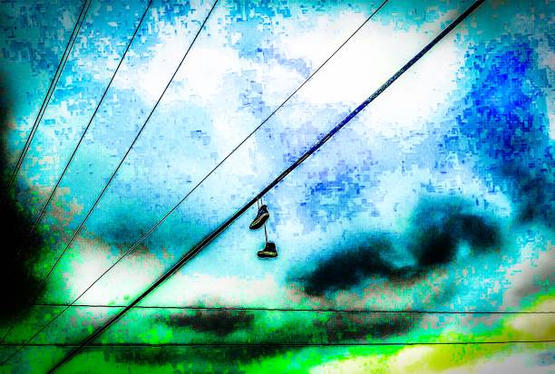shot of shoes hanging off overhead powerlines against a cloudly sky background
