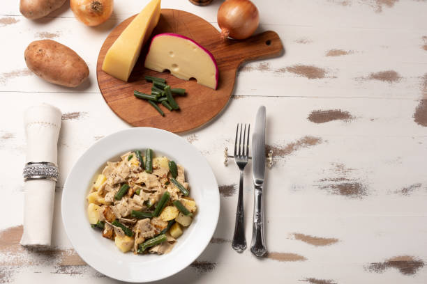 pizzoccheri alla valtellinese casero;  una pasta tradicional de tagliatelle corta típica de la provincia de valtellina, en el norte de italia. placa blanca sobre fondo blanco de madera. luz suave - pizzoccheri homemade tagliatelle italy fotografías e imágenes de stock