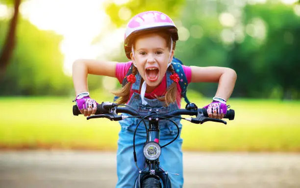 Photo of happy cheerful child girl riding a bike in Park in nature