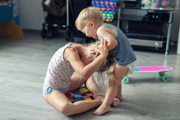 deux petits enfants de frères et sœurs se disputant après avoir joué à la chambre à la maison. pleurant le garçon offensé d'enfant en bas âge se disputant avec la soeur aînée. concept de rivalité familiale et de conflit de génération - conflict face to face child arguing photos et images de collection