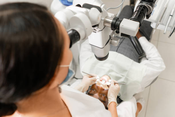 istock Focus on microscope. Young woman dentist treating root canals using microscope in the dental clinic. Man patient lying on dentist chair with open mouth. 1174886160