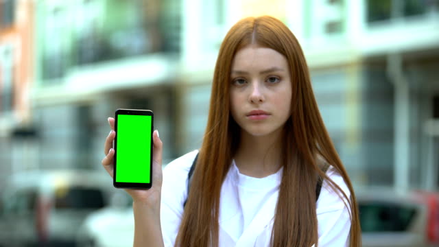 Red-haired girl showing smartphone with green screen, free navigation app