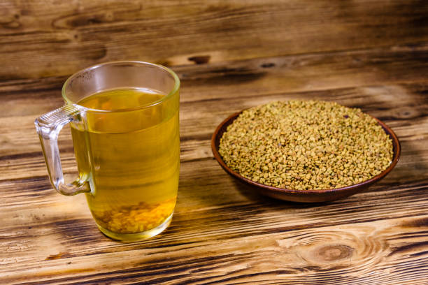 чашка желтого чая (мети дана) и тарелка с семенами пажитника на деревянном столе - 4825 стоковые фото и изображения
