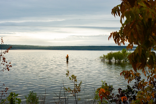 A teen fisherman wading in a lake in soft morning light.