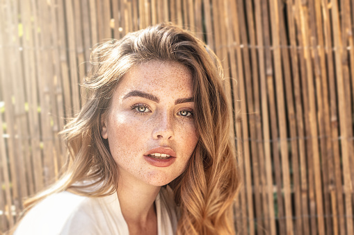 Portrait of young attractive lady with long wavy red hair and freckles on her face. Woman posing on sunny summer day.