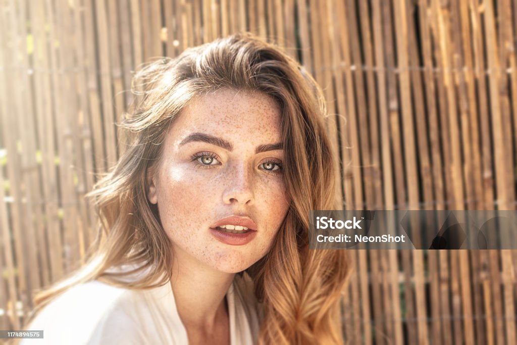 Portrait of young redhead woman with freckles. Portrait of young attractive lady with long wavy red hair and freckles on her face. Woman posing on sunny summer day. Women Stock Photo