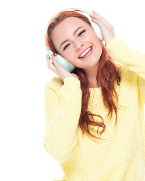 uma pessoa/cintura acima de 18-19 anos de meninas adolescentes caucasianos das mulheres novas do redhead bonito na frente do fundo branco que desgasta as calças de brim que está sorrindo/feliz/alegre/que escuta que está suando e usando auscultadores/mú - 18 19 years audio - fotografias e filmes do acervo