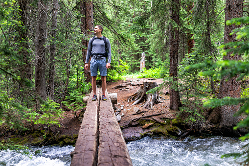 Mountain river stream with man crossing standing in rocky mountains in summer of 2019 on Conundrum Creek trail in Aspen, Colorado with wooden bridge