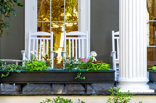Old street historic Garden district in New Orleans, Louisiana with patio garden green plants flowers, white antebellum column and rocking chairs by mansion house