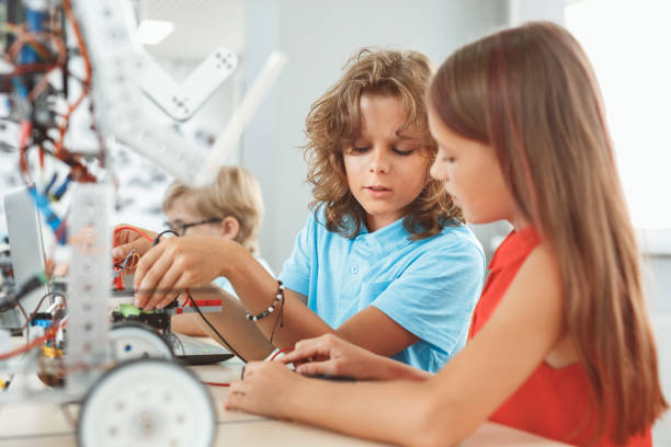 istock Robotics. Children sitting having class working on robot concentrated communicating close-up 1174902725