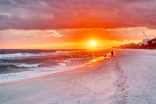 couple looking at colorful sunset in santa rosa beach with pensacola coast in florida panhandle at gulf of mexico ocean waves - florida weather urban scene dramatic sky imagens e fotografias de stock