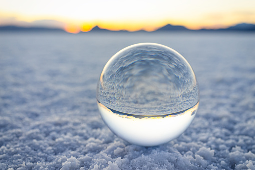 Ground level closeup view on crystal ball with reflection of Bonneville salt flats, mountains at colorful sunset