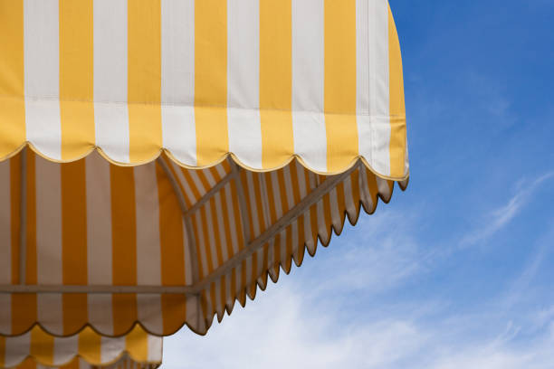 istock yellow and white striped awning with blue sky background. 1174908316