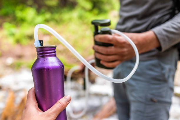 Man and woman couple using water filter on hiking trail river in Colorado to purify drinking water into bottle Man and woman couple using water filter on hiking trail river in Colorado to purify drinking water into bottle giardia lamblia stock pictures, royalty-free photos & images