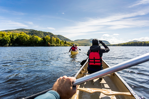 Three People are canoeing on a calm lake on a beautiful sunny day at Parc national du Mont-Tremblant, Quebec, Canada.