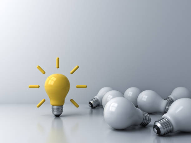 istock Bright idea bulb standing out from the crowd of dim unlit lying white bulbs creative idea concept 1174931869