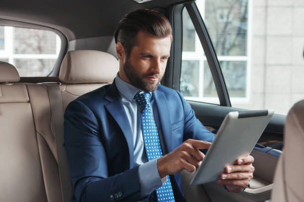 istock Using modern technologies. Young confident and stylish businessman in formal wear is working on digital tablet while sitting on the back seat of his car. 1174933361