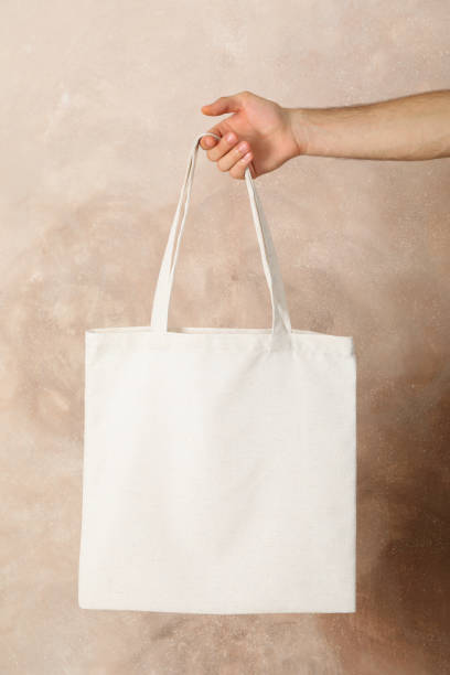 istock Male hand holding tote bag against brown background, empty space 1174942685