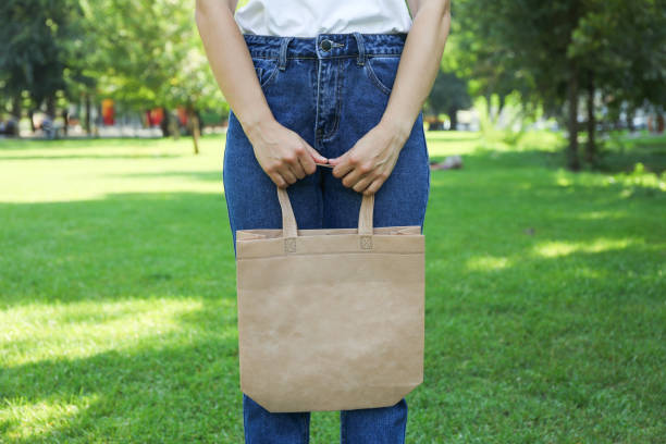 istock Young woman holding tote bag against greenery background, empty space 1174942696