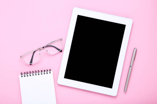 istock Tablet computer with glasses, notepad and pen on pink background 1174942836