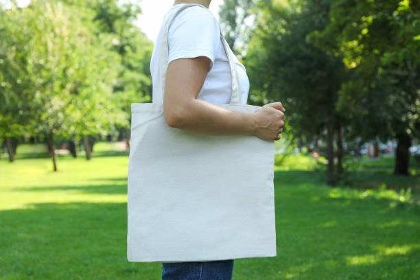 istock Young woman holding tote bag against greenery background, empty space 1174942931