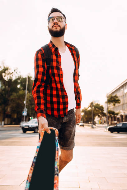 istock guy with a beard in sunglasses, walks with a skateboard at sunset. 1174944876