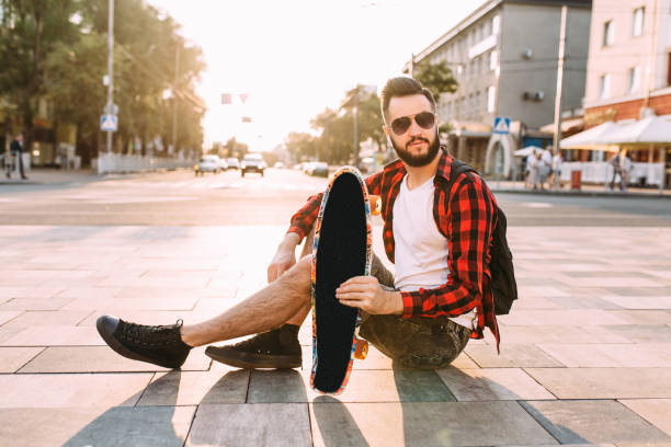 istock guy with a beard in wireless headphones sits in a park with a skateboard 1174945327