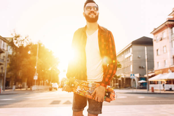 istock guy with a beard in sunglasses, walks with a skateboard at sunset. 1174945975