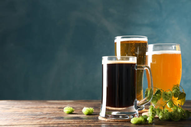 istock Different mugs with beer and hop cones on wooden table, copy space 1174948052