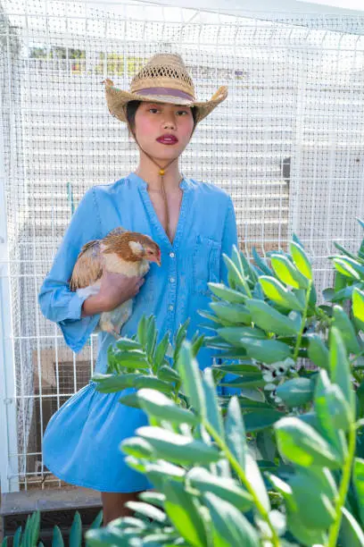 Asian farmer young woman holding hen in hand in front of henhouse outdoor