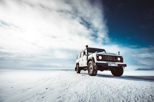 Hofn, Iceland - April 15, 2017: Old white Land Rover Defender 4x4 SUV parked in the snowed road in the center of Westfjords, Iceland. Cloudy day with all the ground full of ice.