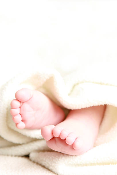 Legs infant baby lying on white bed.