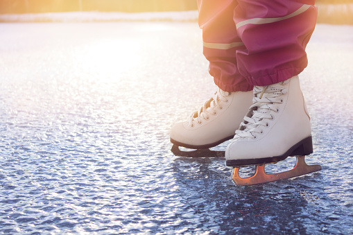Close up view of young 4 year old girl wearing white figure skates, skating on frozen lake in nature outdoors on cold sunny winter day. Hobby concept.