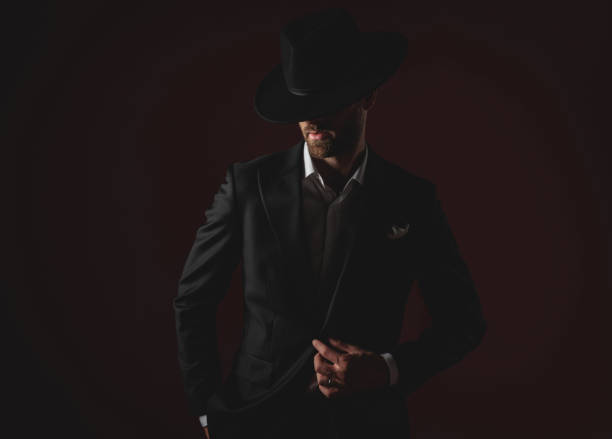 istock attractive young man wearing tuxedo and black hat on black background 1174965790