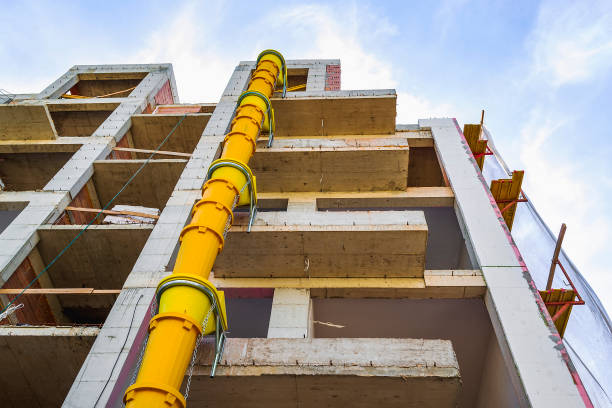 Suspended sections of yellow garbage chute on a facade of building under construction against blue sky with white cloud. stock photo