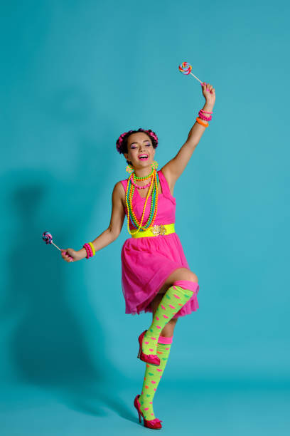 istock Lovely girl with a multi-colored braids hairstyle and bright make-up, posing in studio against a blue background, holding a lollipop in her hand 1174973645